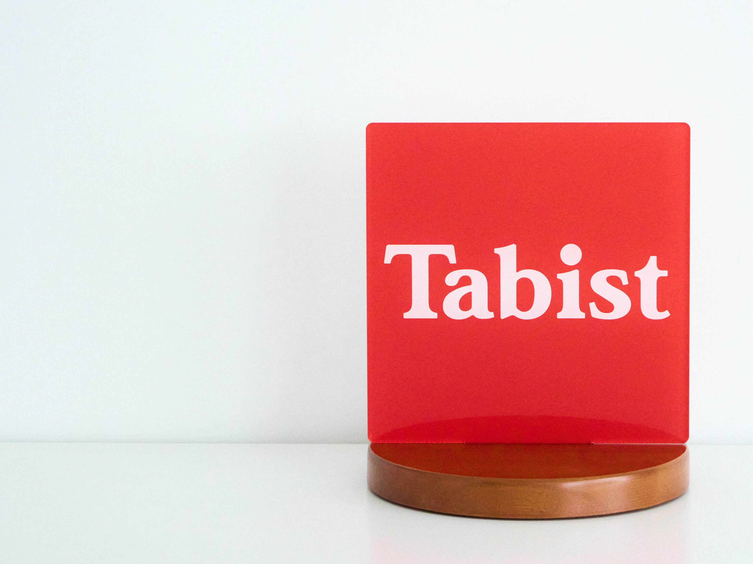 Un panneau rouge portant le mot « Tabist » et fixé sur un socle en bois.