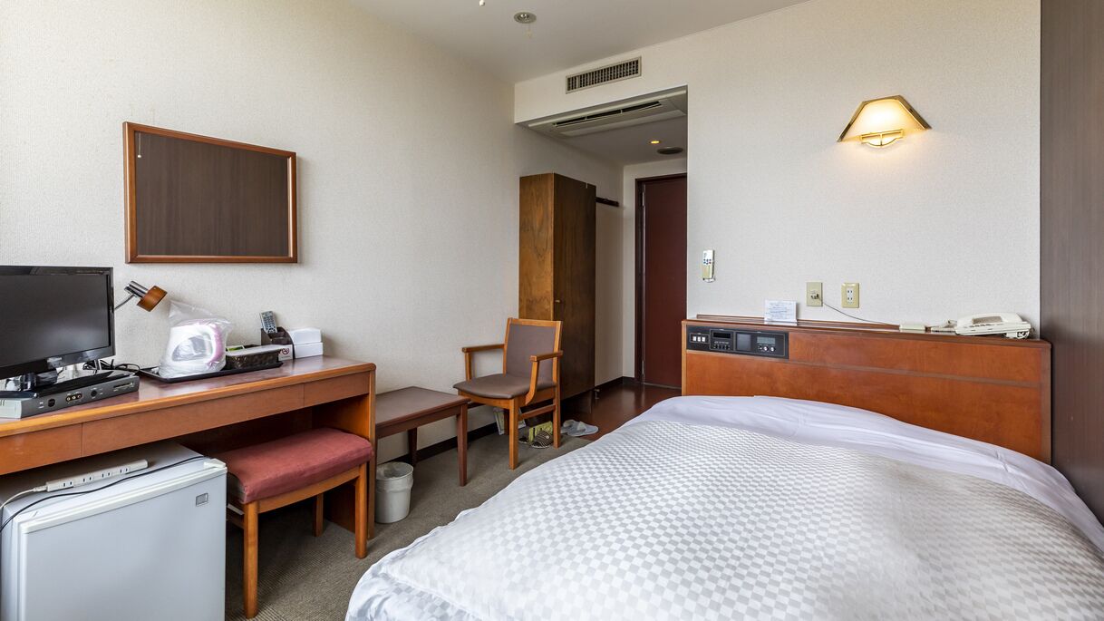Een hotelkamer met een bed, bureau, stoel en een kleine koelkast.