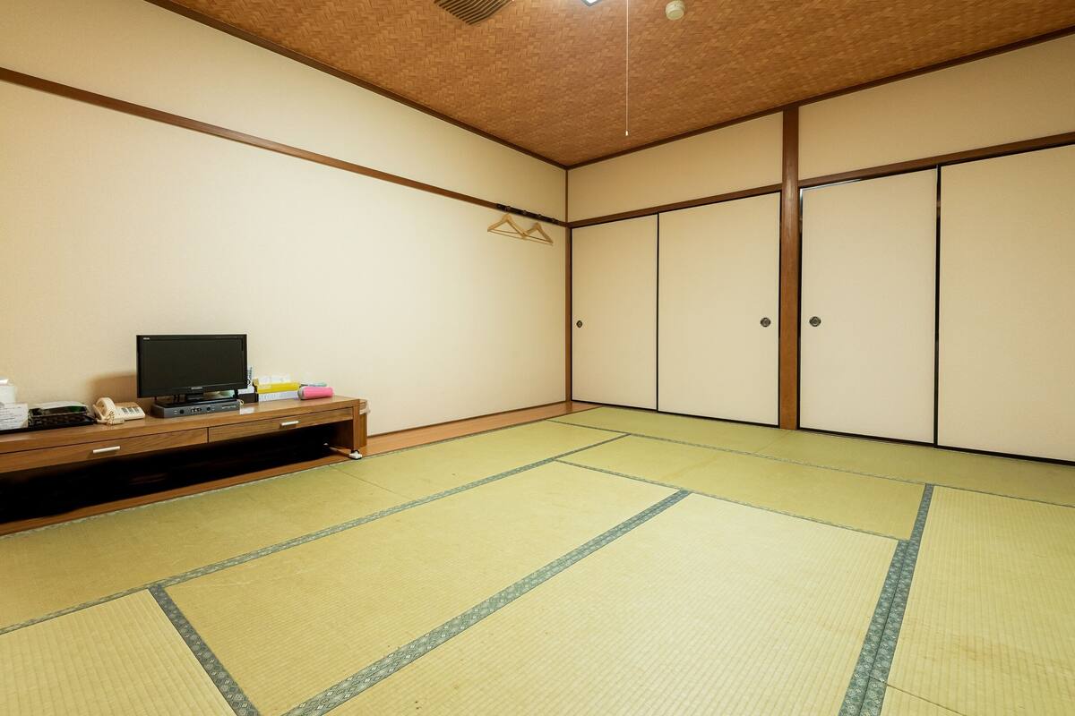 A room with tatami flooring, a television on a wooden cabinet, and sliding doors.