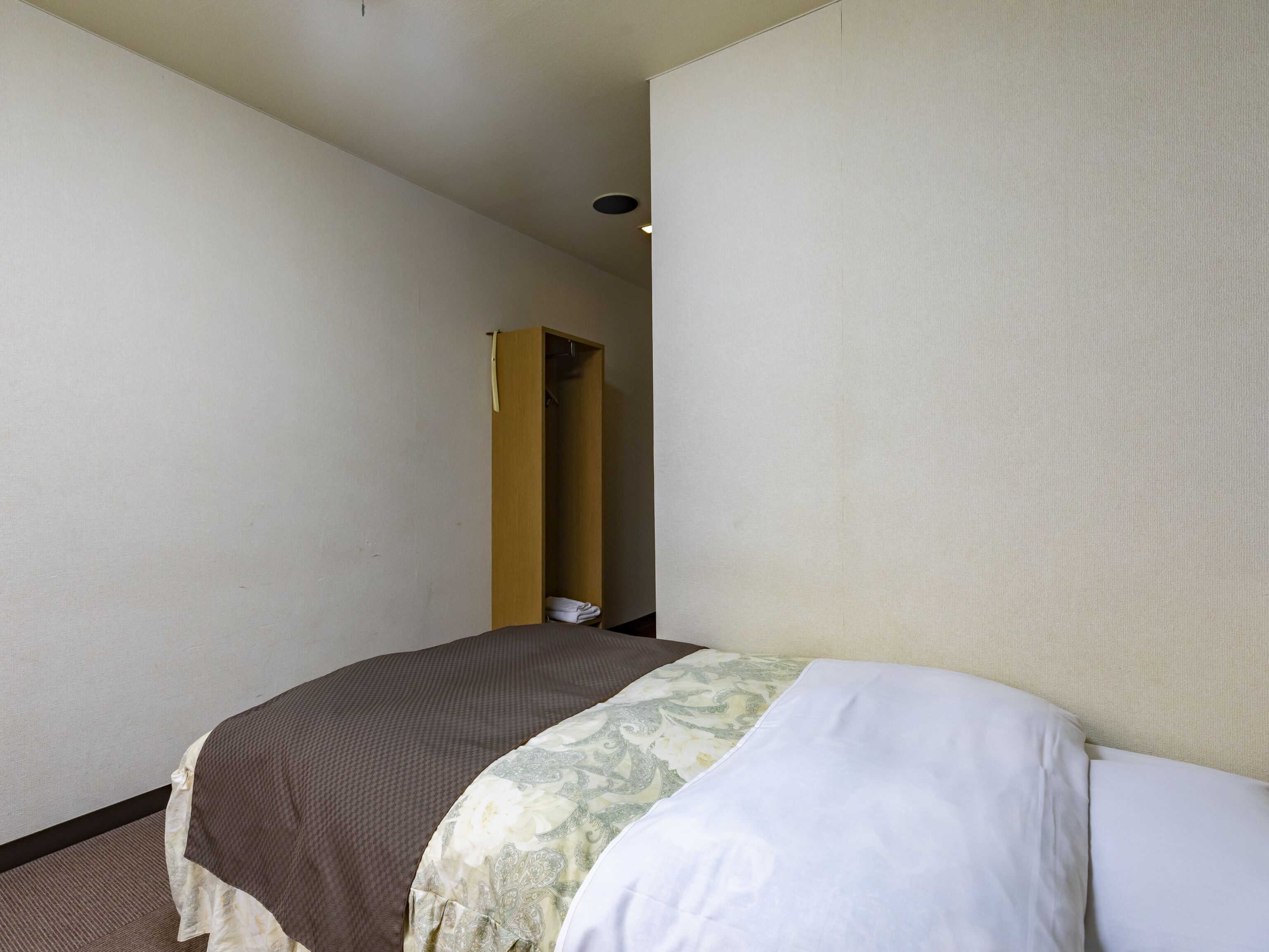 A hotel room with a bed, a wardrobe, and a door leading to another room.