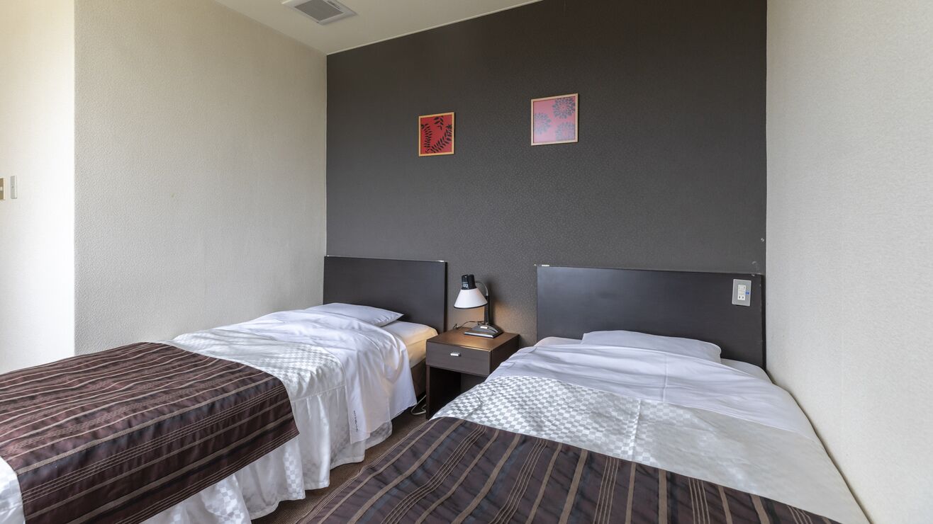 Een hotelkamer met twee enkele bedden, een nachtkastje met een lamp en twee ingelijste foto's aan de muur.