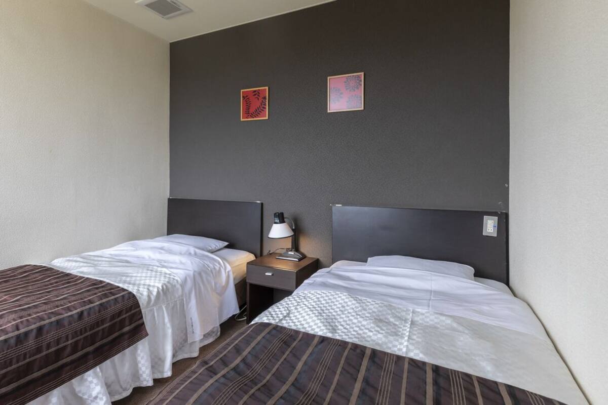 A hotel room with two single beds, a nightstand with a lamp, and two framed pictures on the wall.