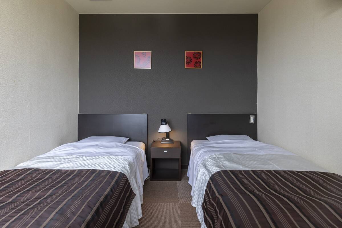 A hotel room with two single beds, a nightstand with a lamp, and two wall-mounted artworks.