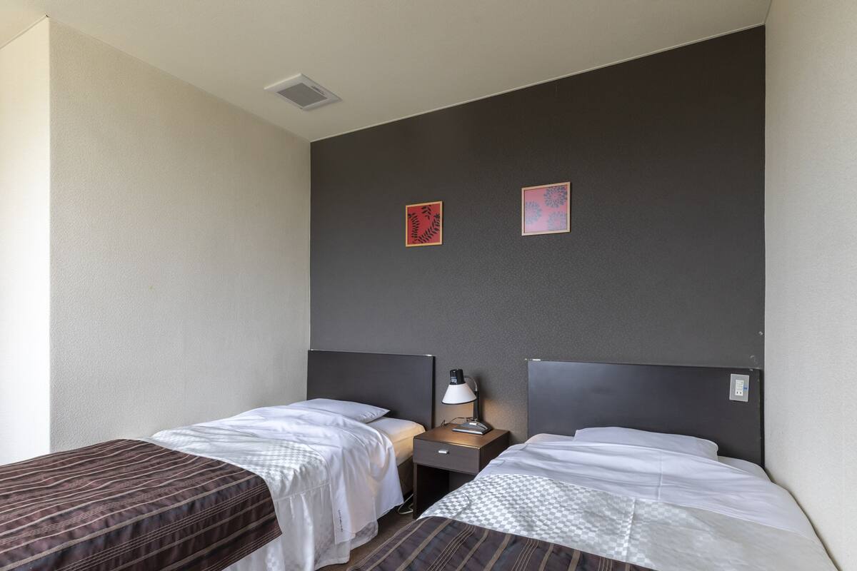 A hotel room with two single beds, a nightstand with a lamp, and two framed pictures on the wall.