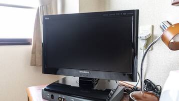 A Mitsubishi TV on a wooden table with a lamp and power cords.