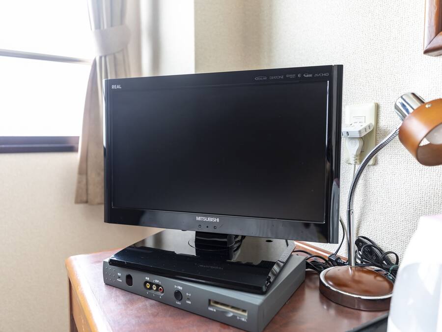 A Mitsubishi TV on a wooden table with a lamp and power cords.