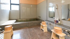 A modern bathroom with a bathtub, wooden stools, a large mirror, and a window.