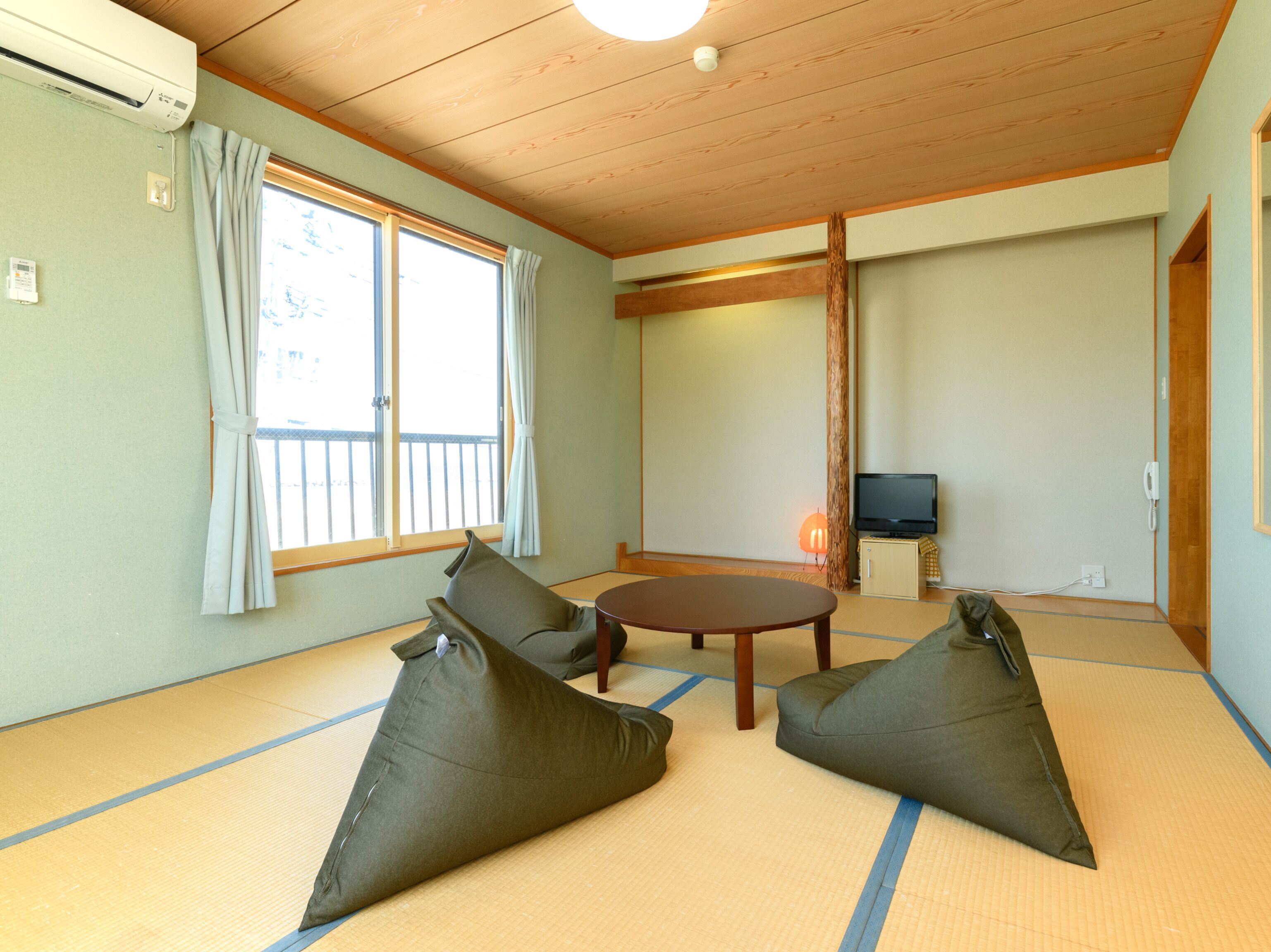 A traditional Japanese room with tatami flooring, a tatami mat table, cushions, a television, and a sliding door.