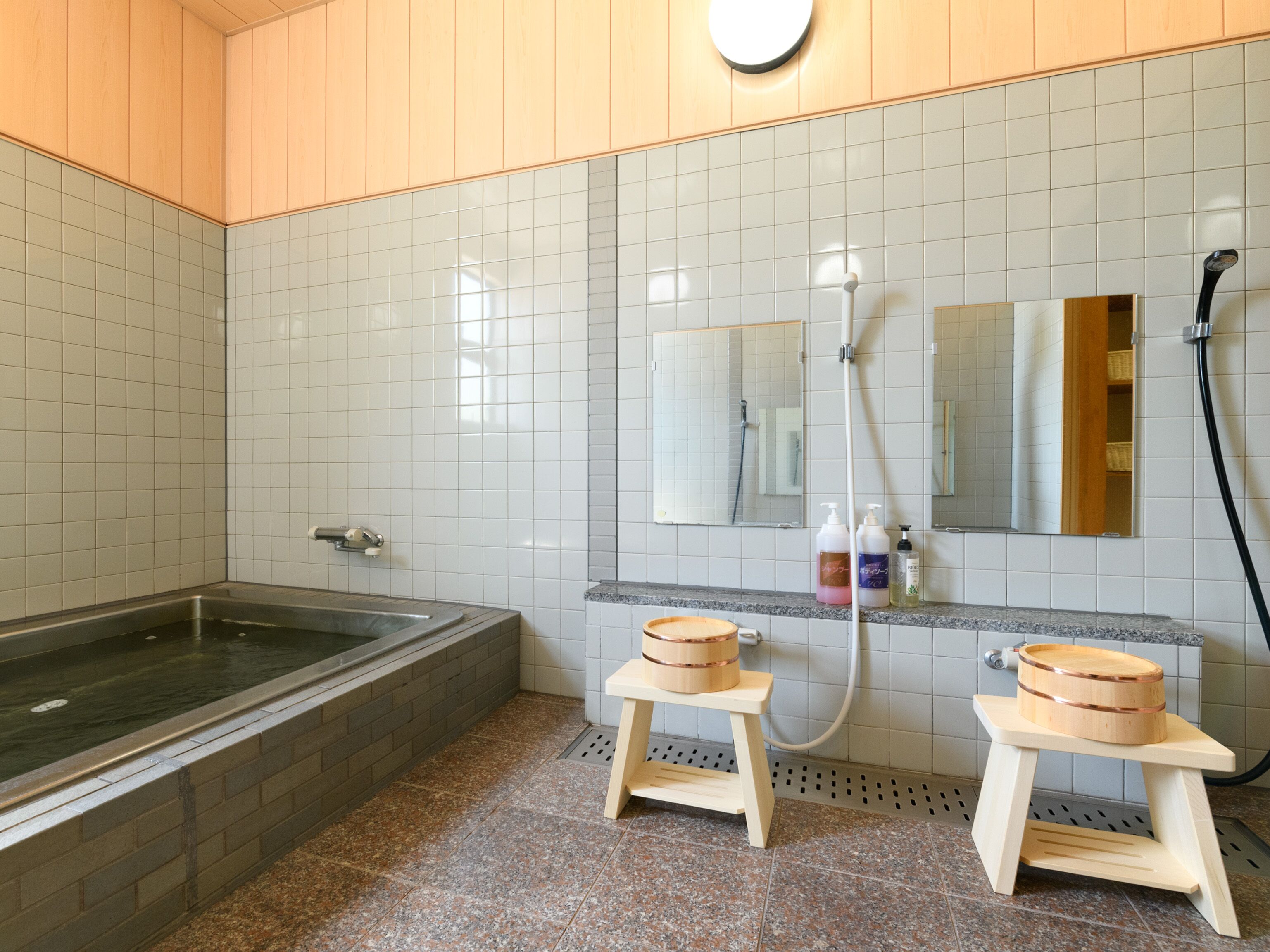 A modern bathroom with a bathtub, two wooden stools, a mirror, and a shower.