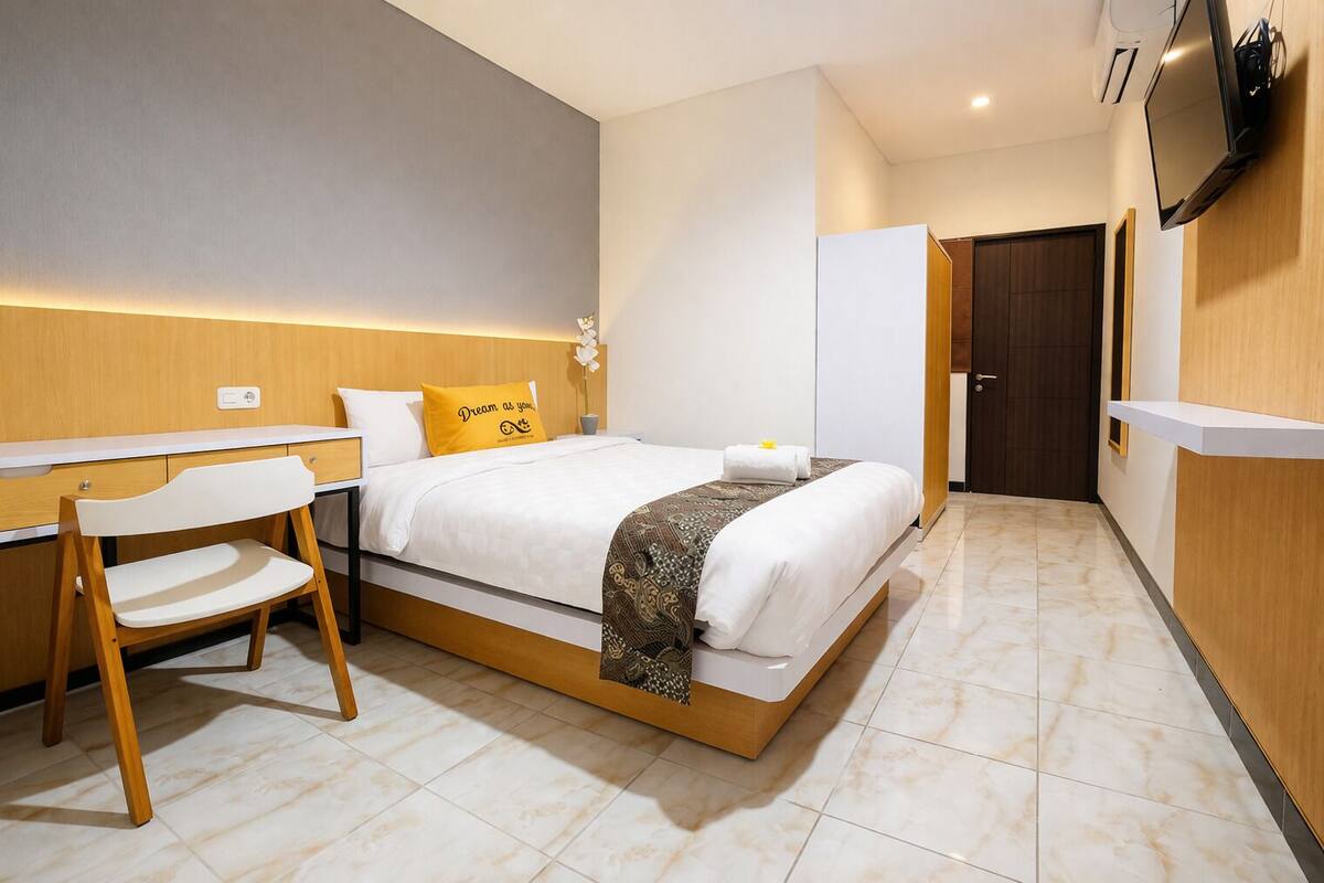 A hotel room with a bed, bedside table, chair, and a TV mounted on the wall.