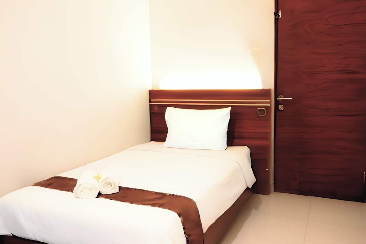 A hotel room with a neatly made bed, a wooden door, and a wall-mounted light fixture.