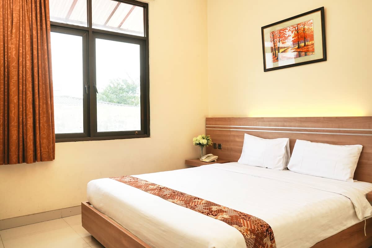 A neatly made bed with a patterned bedspread, a bedside table with a phone and a vase of flowers, and a framed picture on the wall.