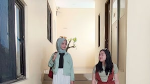 A hallway with a staircase, a potted plant, and a blue suitcase. - Gapura Residence By Sinergi (Semarang)