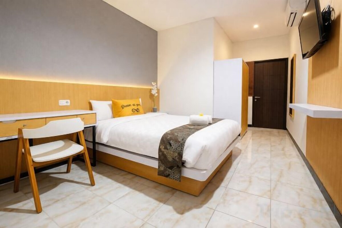 A hotel room with a bed, desk, chair, and a television mounted on the wall.