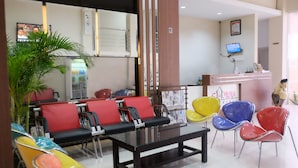 A reception area with a counter, a television, and a seating area with colorful chairs. - Gapura Residence By Sinergi (Semarang)