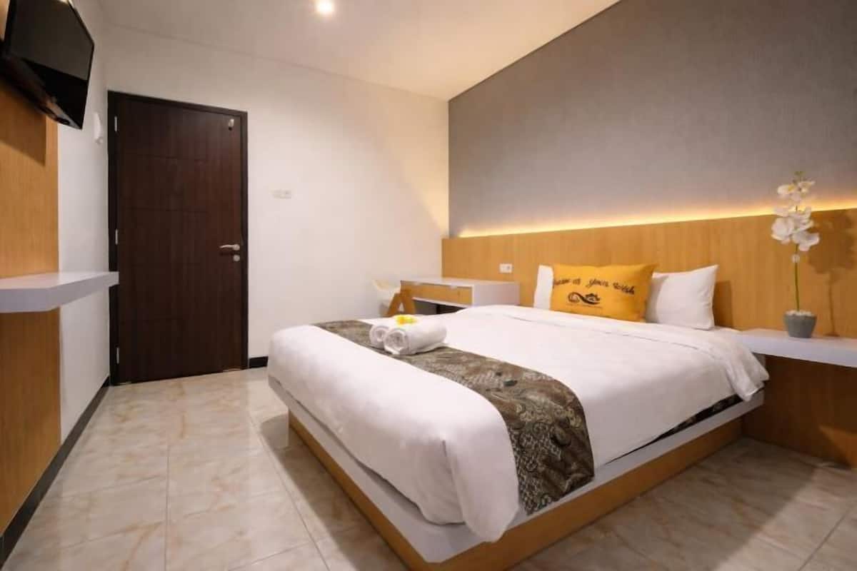 A hotel room with a bed, a bedside table, a TV, and a door.