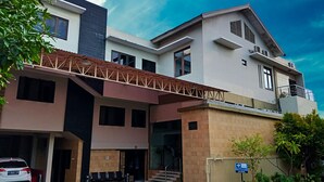A modern multi-story building with a covered entrance, a car parked in the driveway, and a sign indicating a Blue Card Group. - Gapura Residence By Sinergi (Semarang)