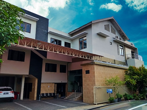 A modern multi-story building with a covered entrance, a car parked in the driveway, and a sign indicating a Blue Card Group.