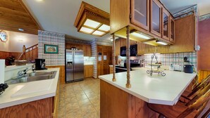 A kitchen with wooden cabinets, a stainless steel refrigerator, a microwave, and a large island with a sink.