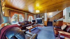 A cozy living room with leather sofas, a fireplace, and a wooden staircase.