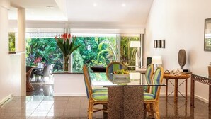 A modern dining area with a glass table, wicker chairs, and a view of lush greenery outside.