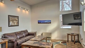 Ein Wohnzimmer mit einem braunen Ledersofa, zwei Holztischen, einem Flachbildfernseher und gerahmten Kunstwerken an den Wänden.