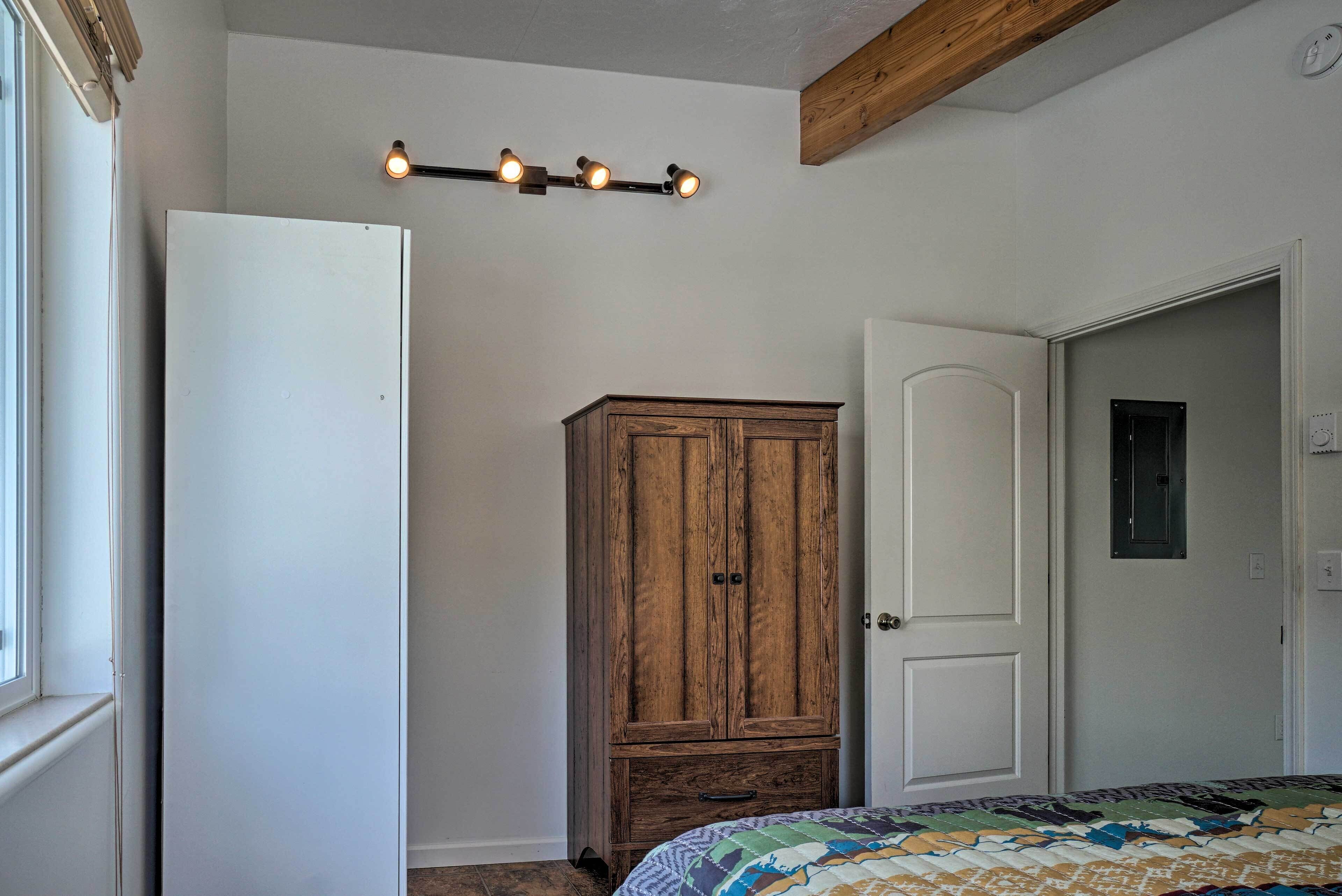 A bedroom with a wooden wardrobe, a bed with a patterned quilt, and a ceiling light fixture.
