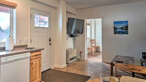 A kitchen with a dishwasher, a flat-screen TV mounted on the wall, and a dining area with a table and chairs. - Homer Hideaway on Fritz Creek! Families Welcome (Homer)