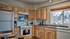 A kitchen with wooden cabinets, a refrigerator, stove, microwave, and dishwasher. There is a window with a view of trees. - Homer Hideaway on Fritz Creek! Families Welcome (Homer)