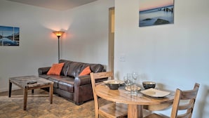A living room with a brown leather sofa, a coffee table, a dining table set with plates, bowls, and glasses, and a lamp. - Homer Hideaway on Fritz Creek! Families Welcome (Homer)