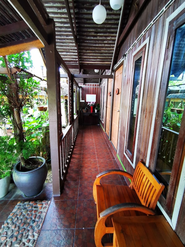 A covered corridor with wooden benches, potted plants, and a tiled floor.