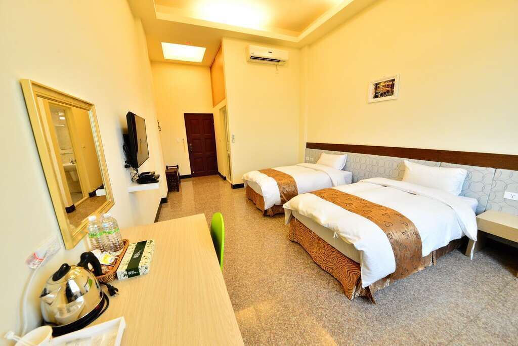 Habitación de hotel con dos camas, un escritorio, un espejo, una televisión y una puerta.