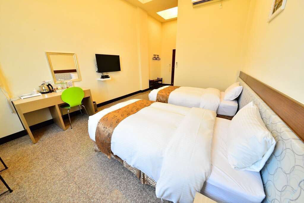 Habitación de hotel con dos camas, un escritorio con silla, televisor de pantalla plana y un espejo.