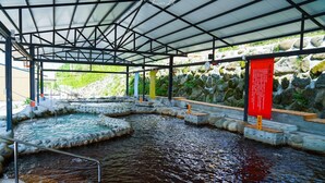 Un espace extérieur abrité avec plusieurs bassins d’eau chaude, des murs en pierre et un panneau d’information rouge.