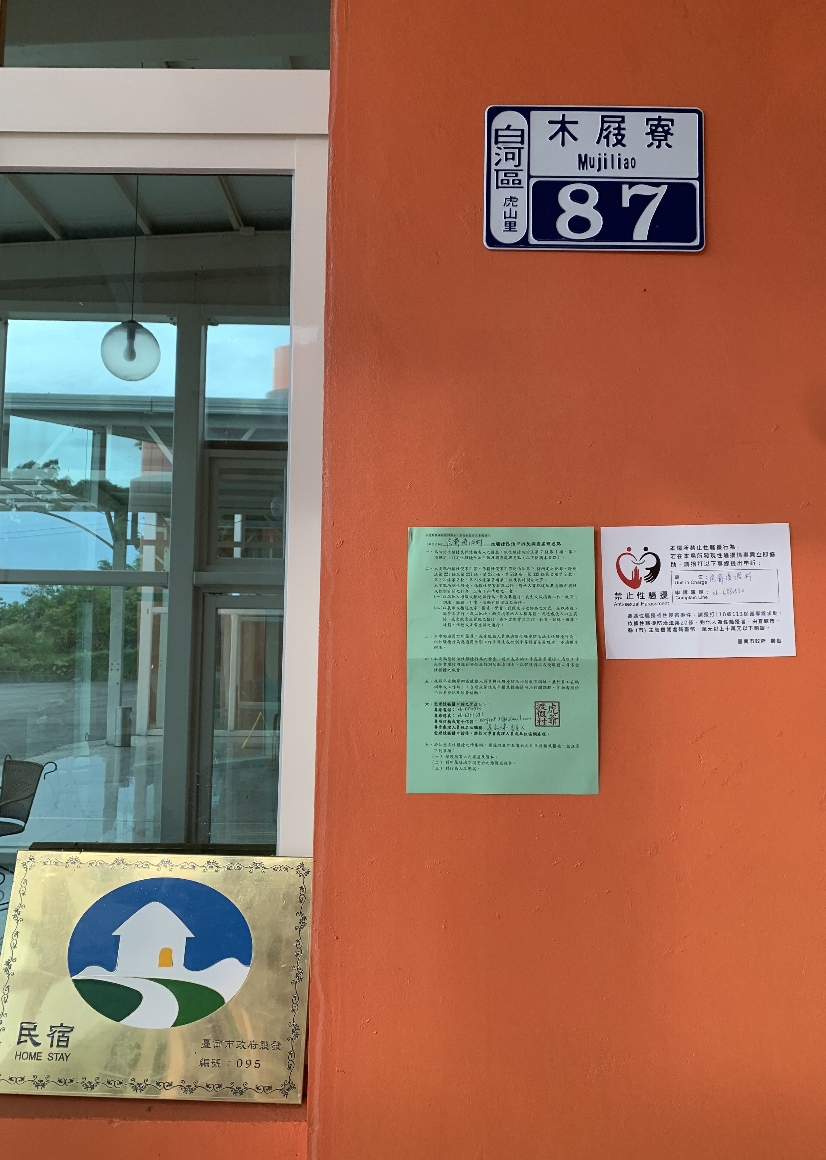 A hotel entrance with a sign indicating room number 87, a green informational sign, and a red anti-sexual harassment notice.