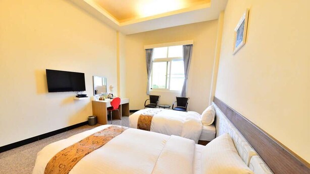 Une chambre d’hôtel avec deux lits, une télévision, un bureau avec une chaise et une fenêtre avec des rideaux.