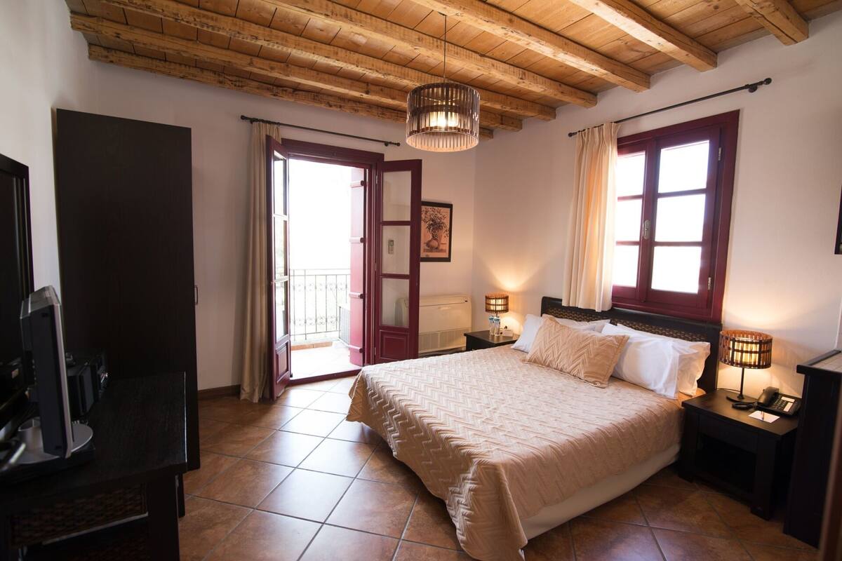 A bedroom with a large bed, wooden ceiling beams, a TV, and a balcony door.