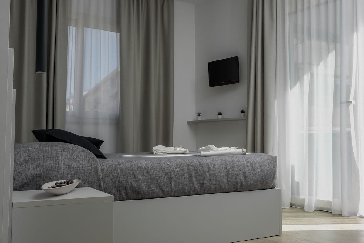 A modern bedroom with a bed, a TV, and a small shelf with plants.