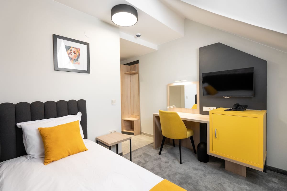 A modern hotel room with a bed, desk, chair, wardrobe, and a TV mounted on the wall.