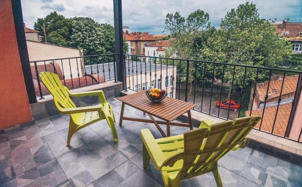 A balcony with two yellow chairs, a small table with a fruit bowl, and a view of the neighborhood.