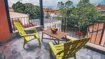 A balcony with two yellow chairs, a small table with a fruit bowl, and a view of the neighborhood.