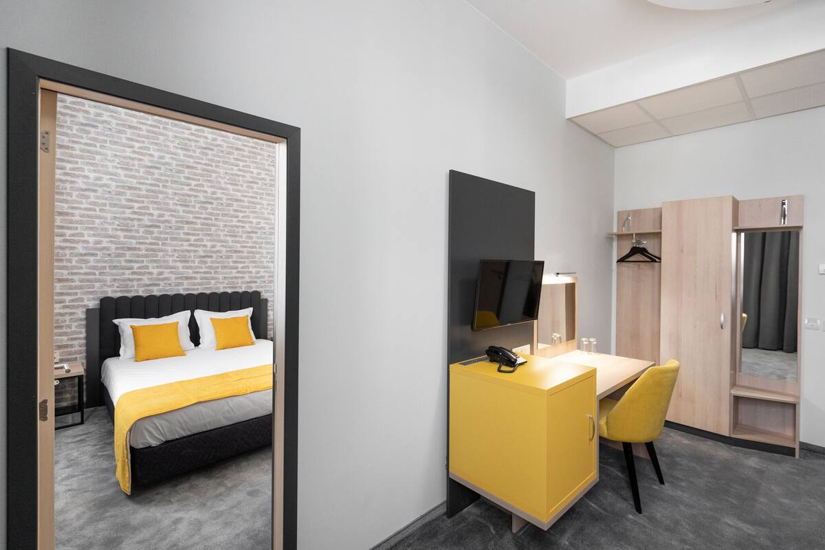 A modern hotel room with a bed, a desk, a chair, a TV, and a wardrobe.