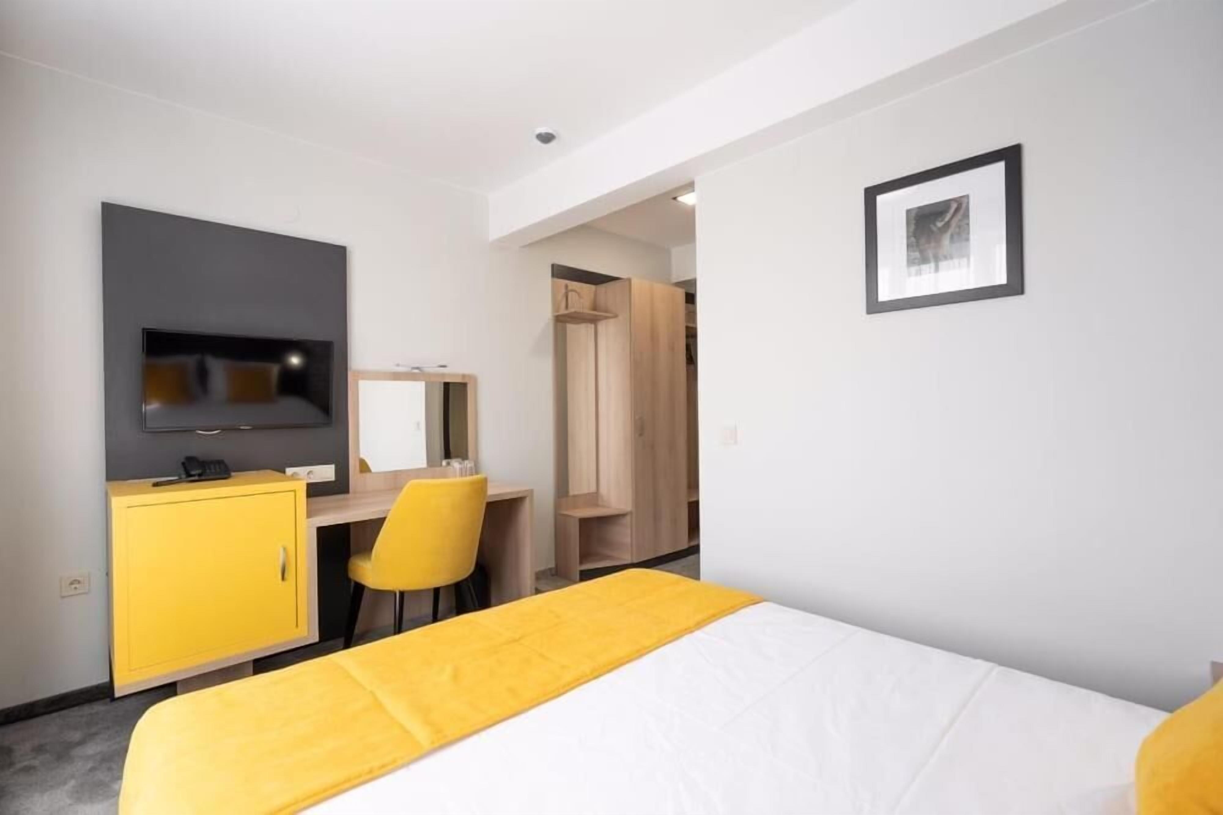 A hotel room with a bed, a desk, a chair, a wardrobe, and a television.