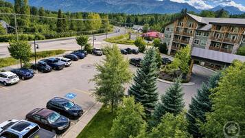 En parkeringsplats med flera bilar, en byggnad med ett rött tak och en bergig bakgrund.