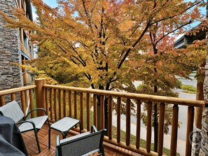 A balcony with a wooden railing, a stone wall, and a view of a tree with autumn leaves. - Fernie 2BR Condo / Hot Tub & Mountain Getaways (Fernie)
