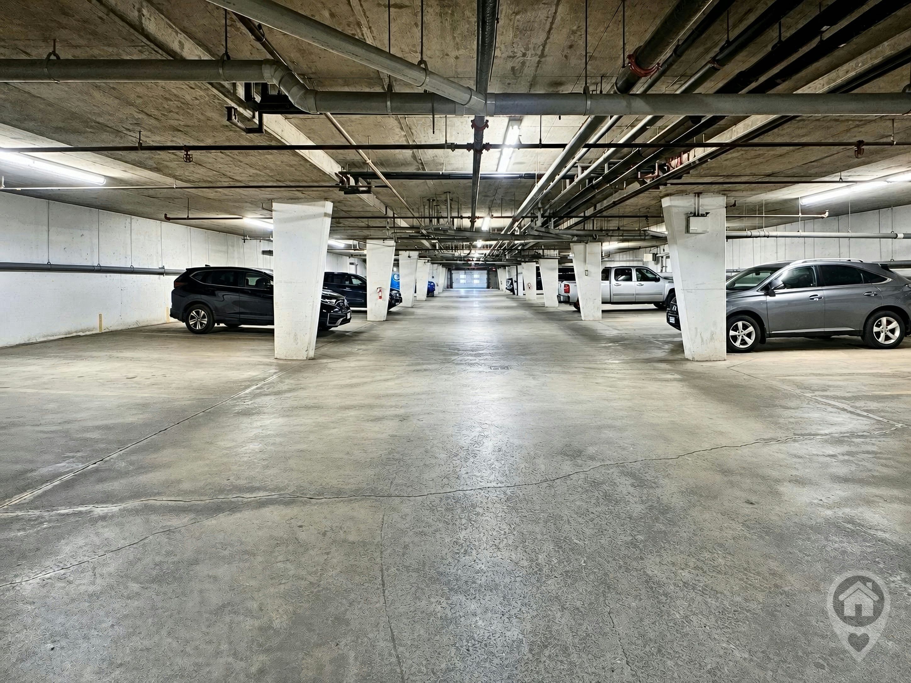Un parking à plusieurs niveaux, avec des piliers en béton, un éclairage fluorescent et des véhicules stationnés dans des emplacements désignés.