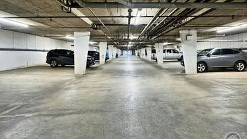 Un parking à plusieurs niveaux, avec des piliers en béton, un éclairage fluorescent et des véhicules stationnés dans des emplacements désignés.