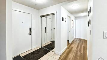 Un couloir aux murs blancs, doté d’un plancher en bois et d’un paillasson noir menant à une porte.