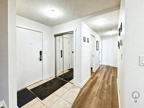 A hallway with white walls, a wooden floor, and a black doormat leading to a door. - Fernie 2BR Condo / Hot Tub & Mountain Getaways (Fernie)