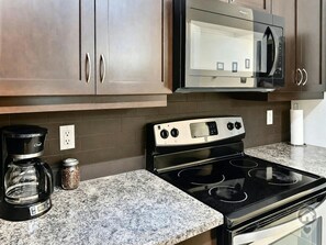 A kitchen with dark wooden cabinets, a stainless steel microwave, a gas stove, and a coffee maker. - Fernie 2BR Condo / Hot Tub & Mountain Getaways (Fernie)